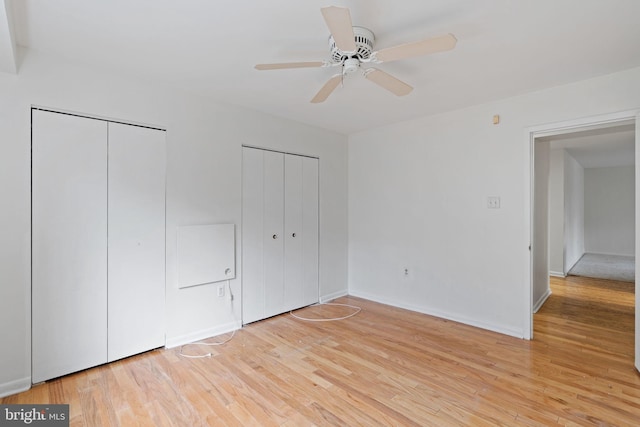 unfurnished bedroom with light wood finished floors, ceiling fan, baseboards, and two closets