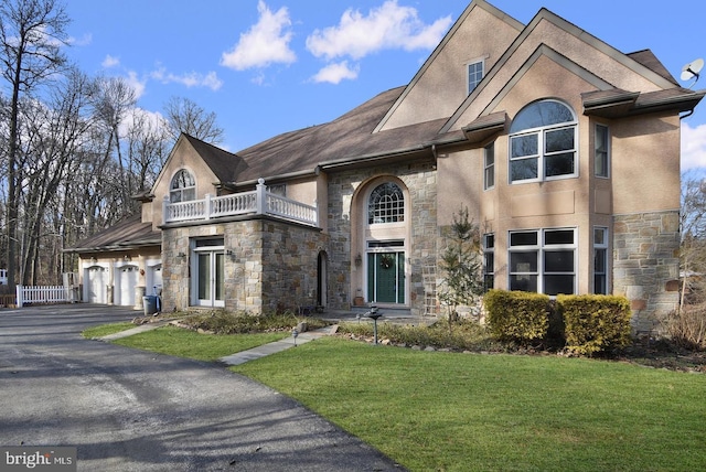 view of front facade with stucco siding, driveway, a front yard, a garage, and a balcony