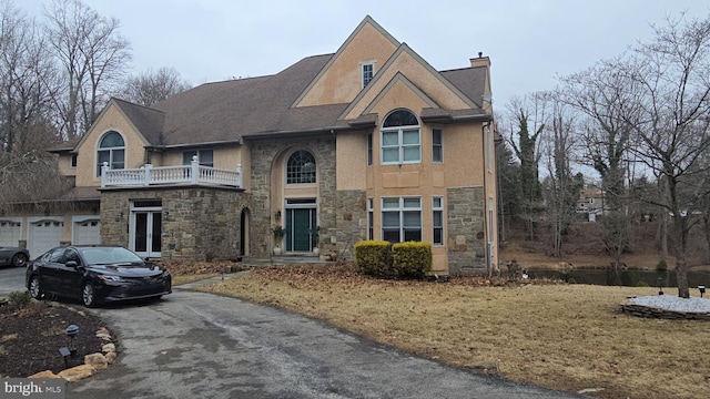 traditional home featuring a balcony, stone siding, driveway, and a chimney