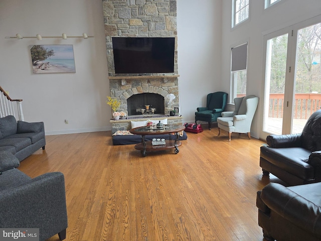 living area featuring wood finished floors, baseboards, a stone fireplace, stairs, and a towering ceiling