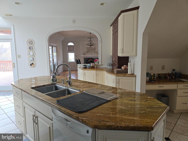 kitchen featuring an island with sink, a fireplace, arched walkways, white dishwasher, and a sink