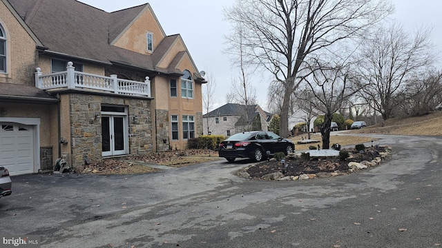 view of property exterior with aphalt driveway, a balcony, a garage, and stone siding