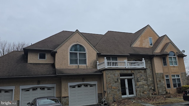 view of front of house with a balcony, stucco siding, a shingled roof, a garage, and stone siding