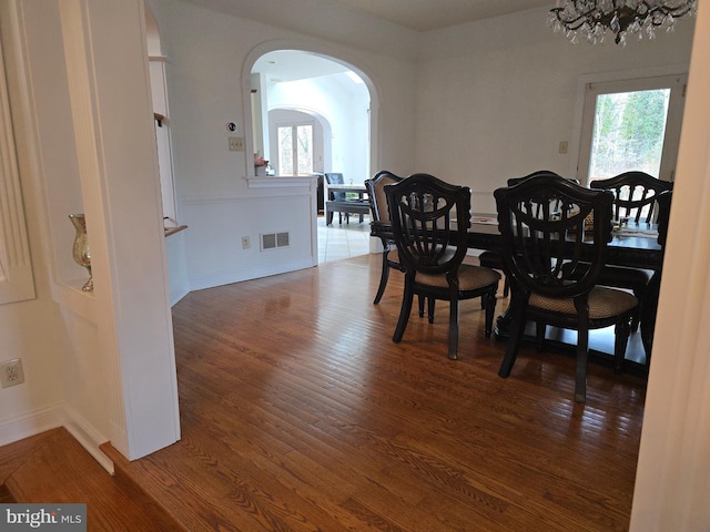 dining space featuring visible vents, baseboards, a chandelier, wood finished floors, and arched walkways