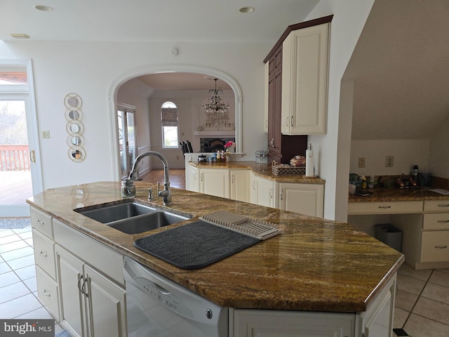 kitchen with light tile patterned flooring, a kitchen island with sink, arched walkways, a sink, and dishwasher