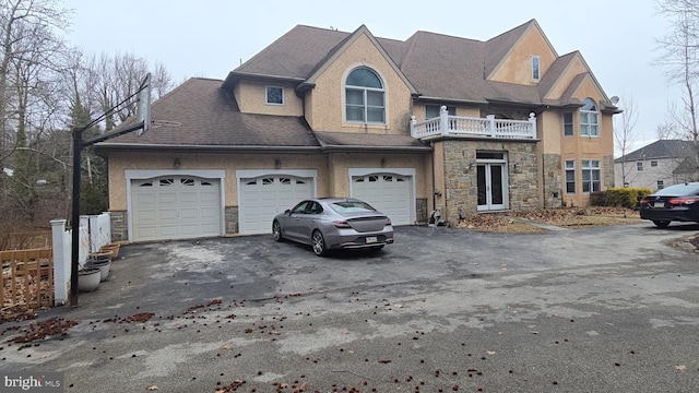 view of front facade with aphalt driveway, a balcony, stone siding, and stucco siding