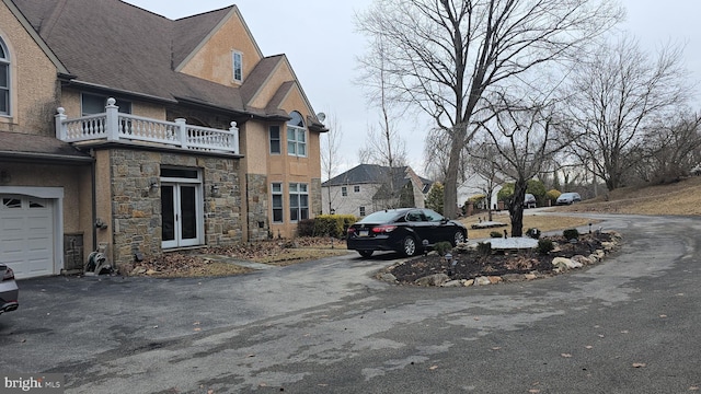 exterior space featuring stone siding, a garage, driveway, and a balcony