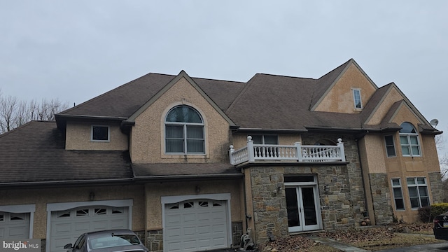 multi unit property with stone siding, stucco siding, an attached garage, and a balcony