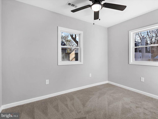 carpeted spare room featuring a healthy amount of sunlight, visible vents, ceiling fan, and baseboards