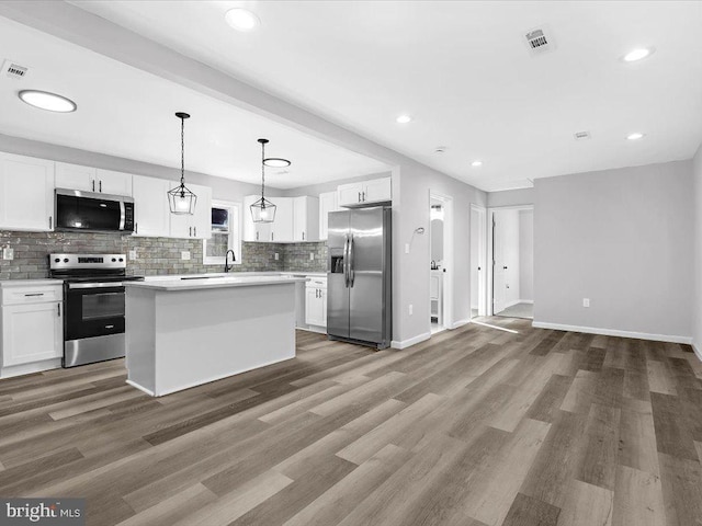 kitchen featuring appliances with stainless steel finishes, white cabinetry, backsplash, and wood finished floors