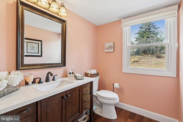 half bathroom with toilet, vanity, baseboards, and wood finished floors