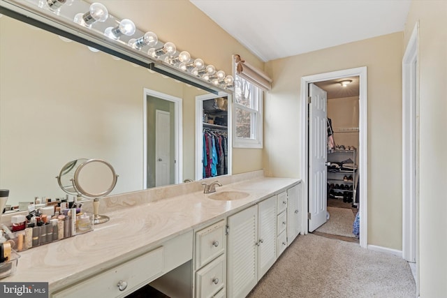 full bath with baseboards, a walk in closet, and vanity