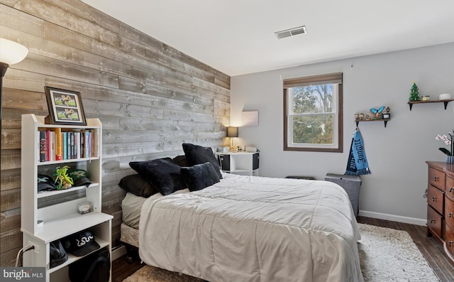 bedroom featuring wooden walls, baseboards, visible vents, an accent wall, and wood finished floors