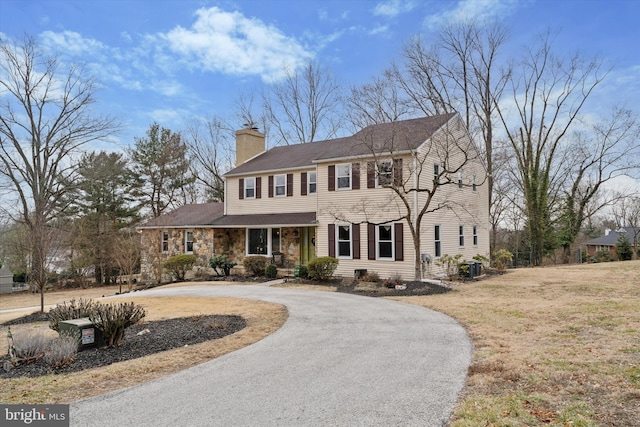 view of front of property with stone siding, curved driveway, and a chimney