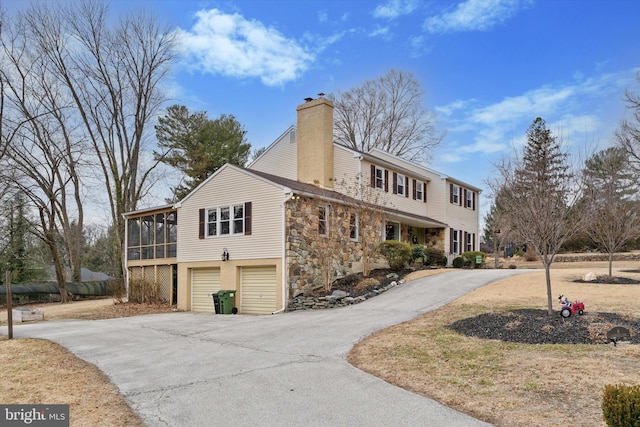 view of front of home featuring aphalt driveway, a chimney, a sunroom, a garage, and stone siding