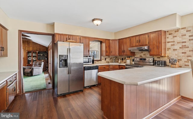 kitchen with dark wood finished floors, stainless steel appliances, light countertops, a peninsula, and under cabinet range hood