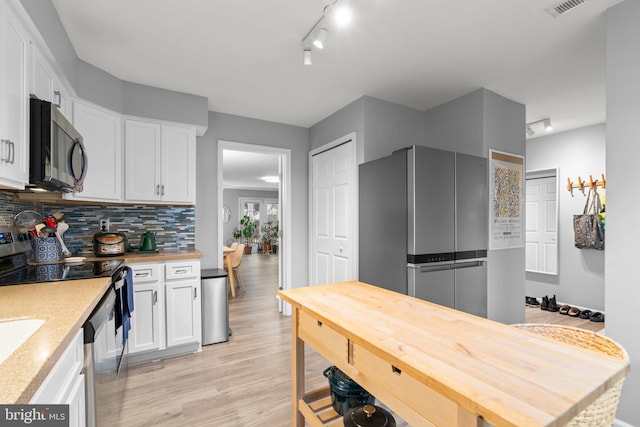 kitchen featuring white cabinets, light wood-style flooring, appliances with stainless steel finishes, light countertops, and backsplash