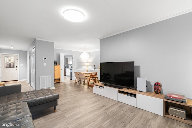 living area with crown molding, baseboards, visible vents, and light wood-style floors