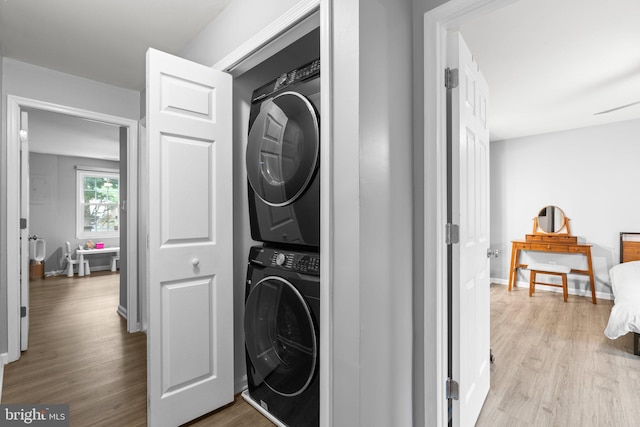 laundry area with stacked washer / drying machine, laundry area, baseboards, and wood finished floors