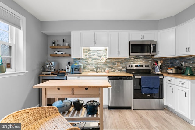 kitchen featuring white cabinets, decorative backsplash, appliances with stainless steel finishes, open shelves, and a sink