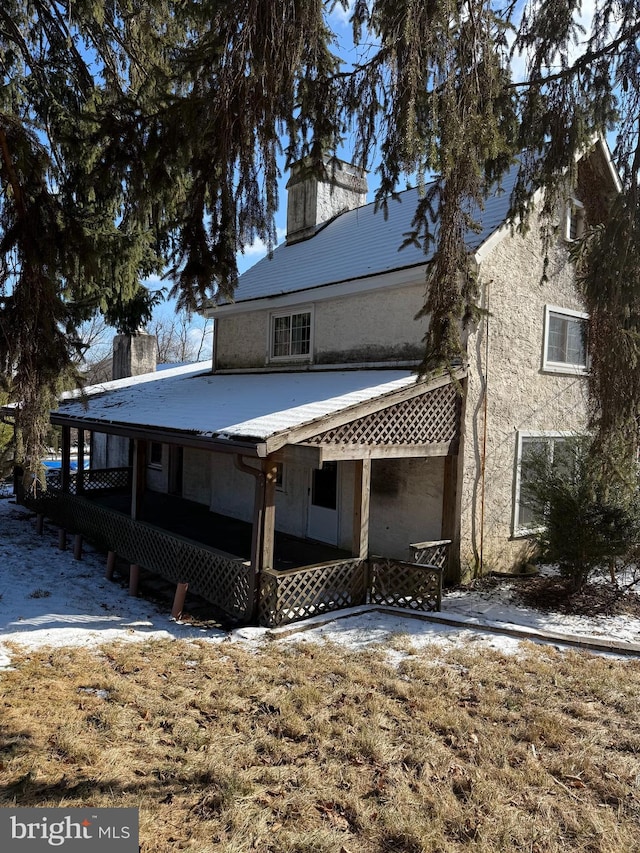 rear view of property with a chimney and stucco siding