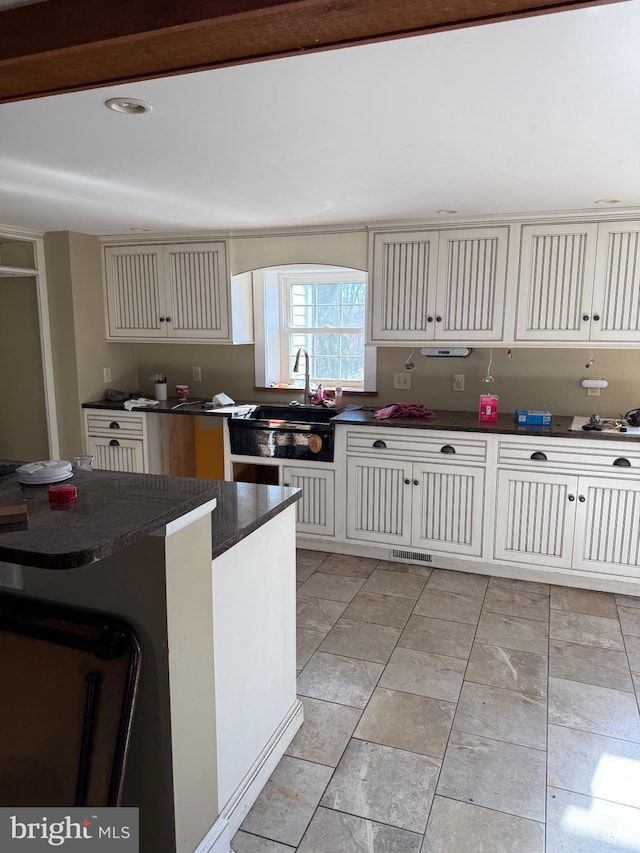 kitchen featuring dark countertops, cream cabinets, visible vents, and a sink