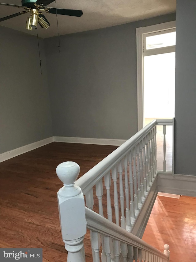 stairway featuring wood finished floors, a ceiling fan, and baseboards