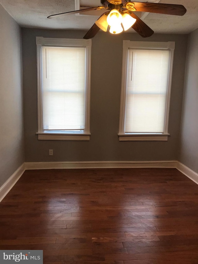 unfurnished room with dark wood-style floors, ceiling fan, a textured ceiling, and baseboards