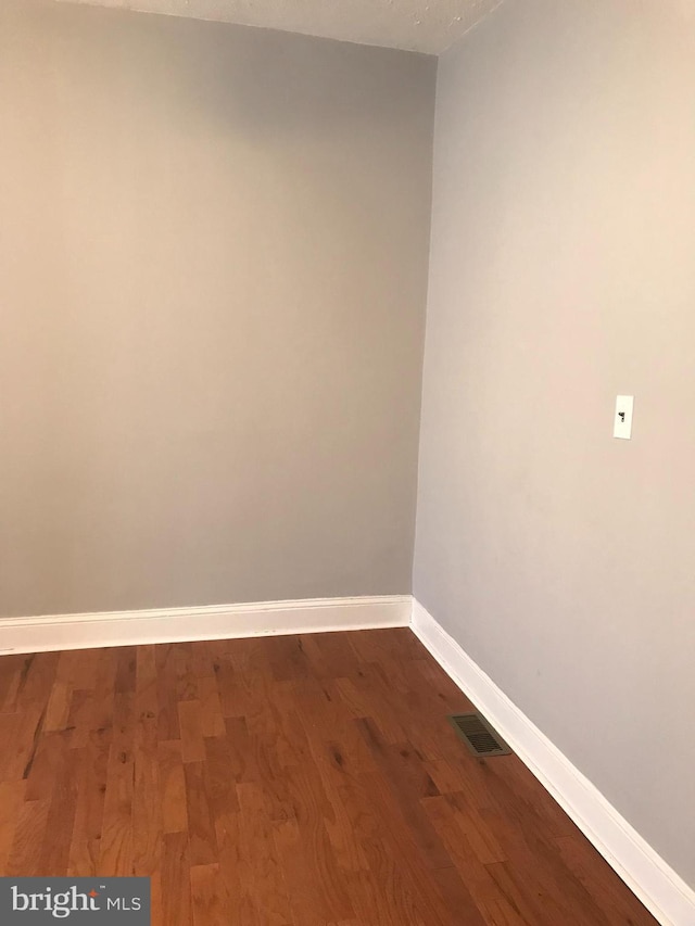 spare room featuring dark wood finished floors, visible vents, and baseboards