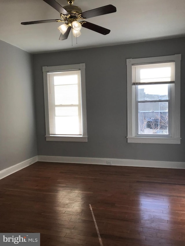 empty room featuring baseboards, dark wood-style flooring, and a wealth of natural light