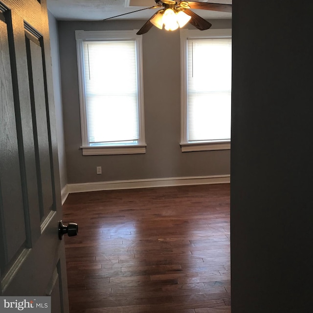 unfurnished room with dark wood-style floors, ceiling fan, and baseboards