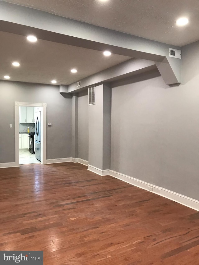 finished below grade area featuring visible vents, wood finished floors, freestanding refrigerator, and baseboards