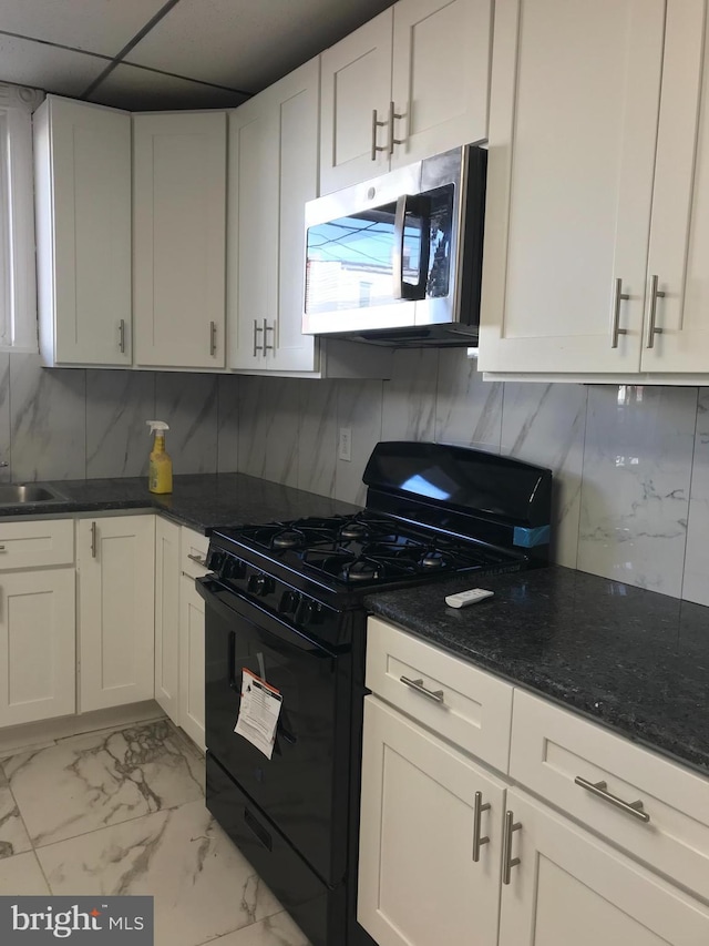 kitchen featuring marble finish floor, stainless steel microwave, black gas range oven, decorative backsplash, and white cabinetry