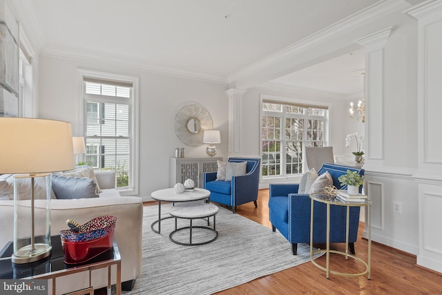 living area featuring ornamental molding, decorative columns, a chandelier, and wood finished floors