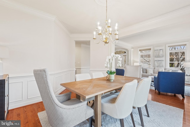 dining area featuring an inviting chandelier, crown molding, a wainscoted wall, a decorative wall, and light wood finished floors