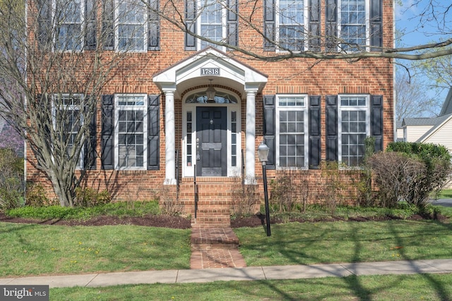 doorway to property with brick siding and a lawn