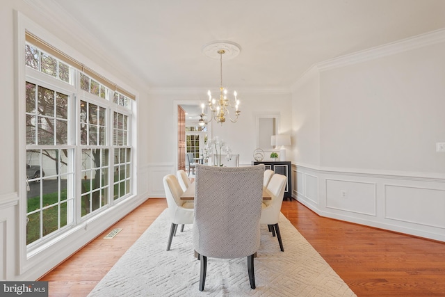 dining space with visible vents, a decorative wall, ornamental molding, a chandelier, and light wood-style flooring