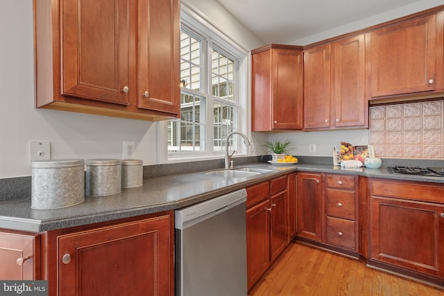 kitchen featuring a sink, stainless steel dishwasher, dark countertops, and light wood-style floors