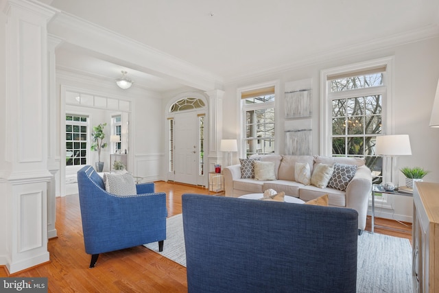 living area featuring crown molding, a wainscoted wall, ornate columns, and light wood-type flooring
