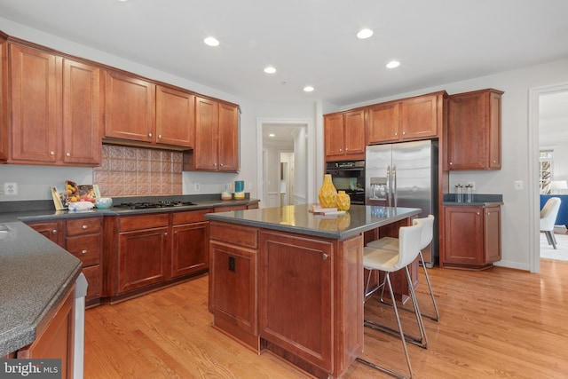 kitchen featuring light wood-style floors, stainless steel fridge with ice dispenser, a kitchen bar, gas stovetop, and black oven