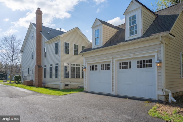 view of front facade with roof with shingles, a chimney, a garage, and aphalt driveway