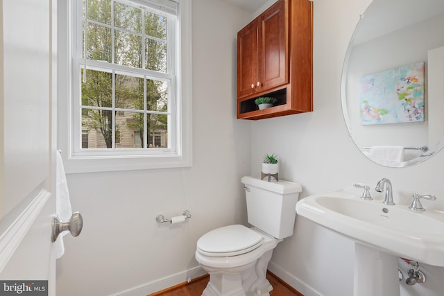 half bath with toilet, wood finished floors, a sink, and baseboards