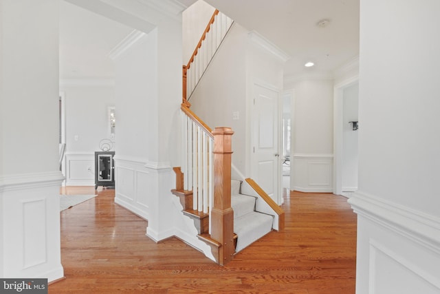 stairs with a decorative wall, a wainscoted wall, wood finished floors, and crown molding