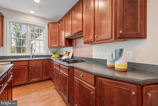 kitchen with light wood-style floors, gas stovetop, a sink, and dark countertops