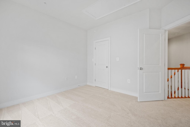 carpeted spare room featuring attic access and baseboards