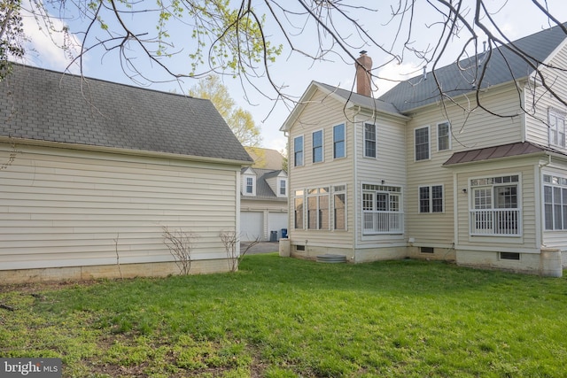 rear view of house featuring a yard, a garage, crawl space, a chimney, and an outbuilding
