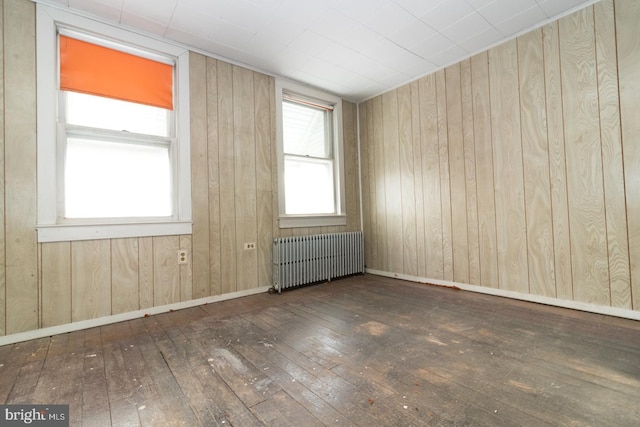 empty room featuring radiator, wood-type flooring, wooden walls, and baseboards