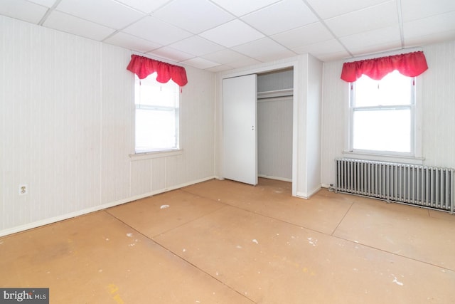 unfurnished bedroom with radiator heating unit, multiple windows, and a drop ceiling