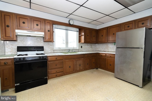 kitchen featuring under cabinet range hood, a sink, light countertops, freestanding refrigerator, and gas stove