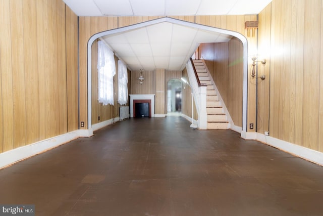 unfurnished living room with arched walkways, wooden walls, a fireplace, baseboards, and stairs